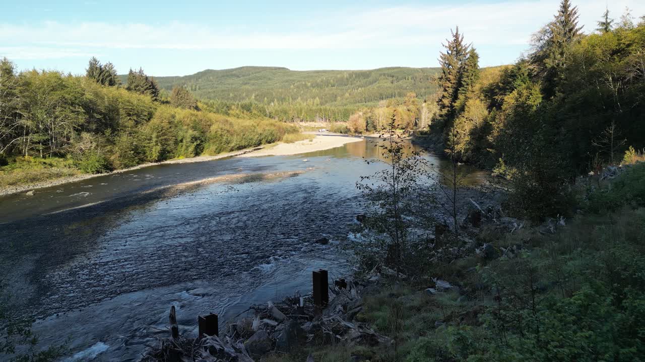 Drone footage soaring over a peaceful riverbend surrounded by dense evergreen forest and rolling hills in the Pacific Northwest