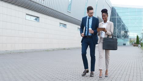 african american businesswoman and caucasian businessman reading something on a tablet and walking down the street