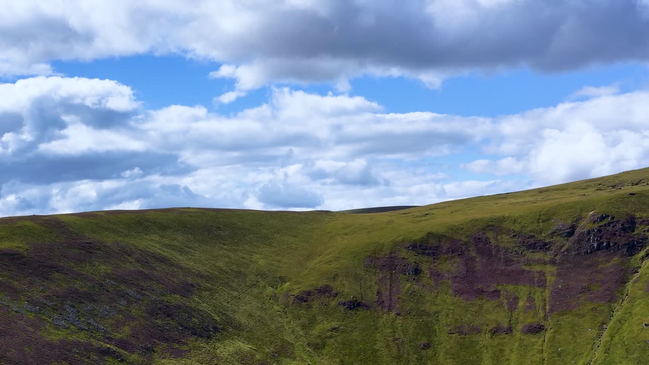 Camera slowly pans across green mountain ridge, dramatic clouds, natural daylight, wide scenic landscape