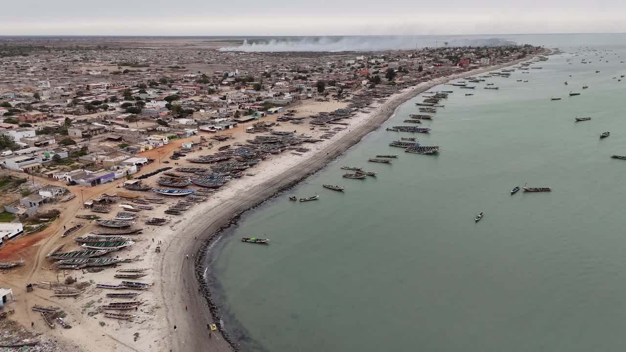 Wide aerial panorama of Joal Fadiouth, Senegal, capturing the coastline, sandy beach, and fishing boats scattered along the Atlantic Ocean shore