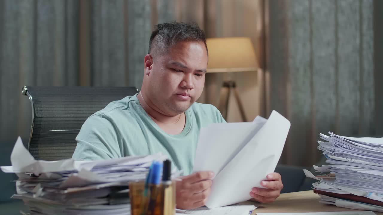 primer plano de un hombre gordo asiático estirándose mientras trabaja duro con documentos en la oficina