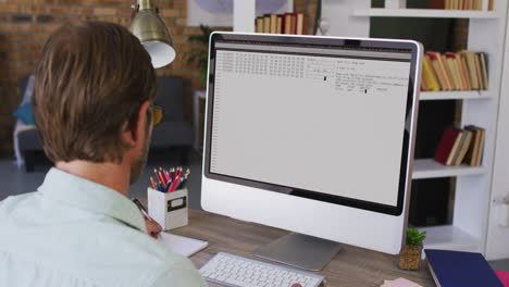 hombre caucásico sentado en un escritorio viendo el procesamiento de datos de codificación en la pantalla de la computadora