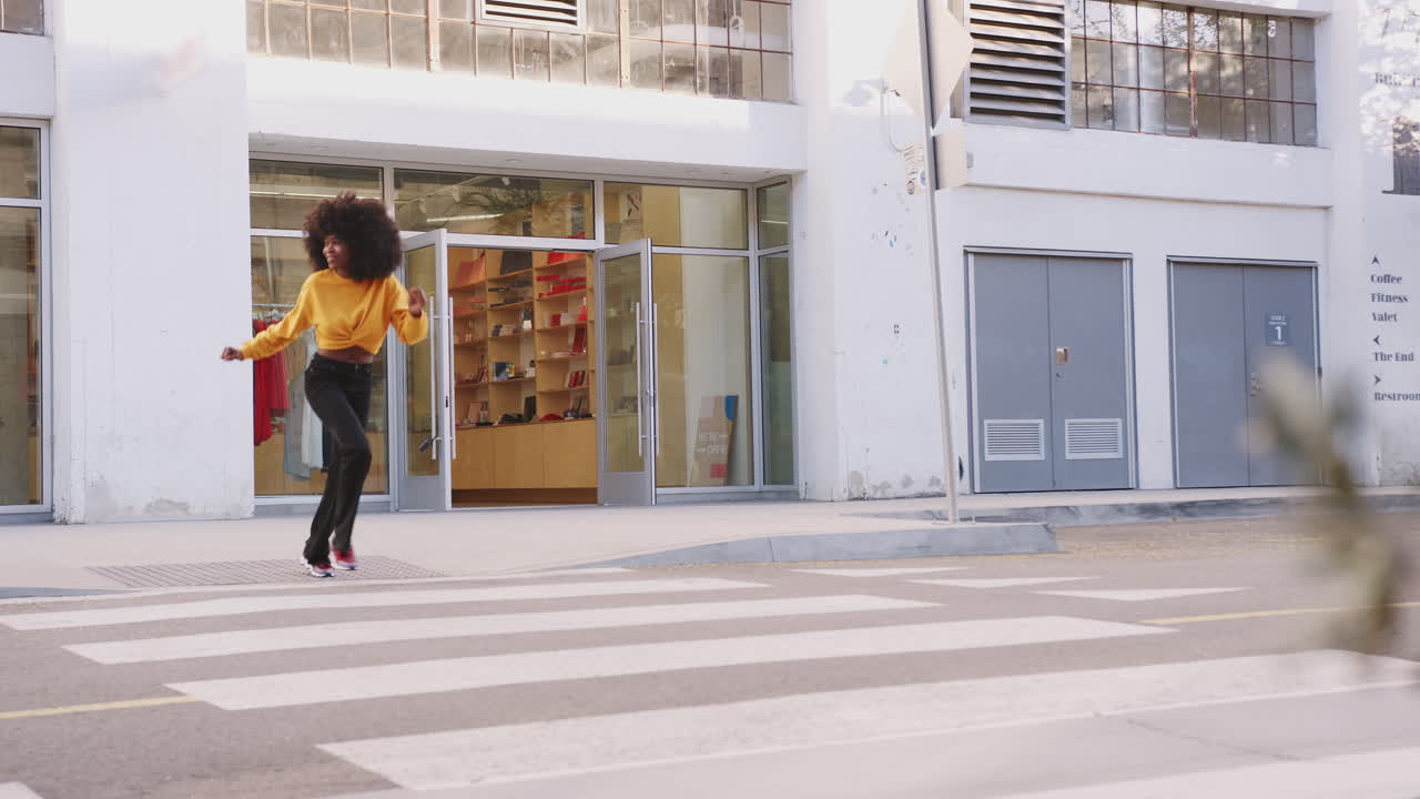 Fashionable young black woman with afro hair running across the street, full length, close up