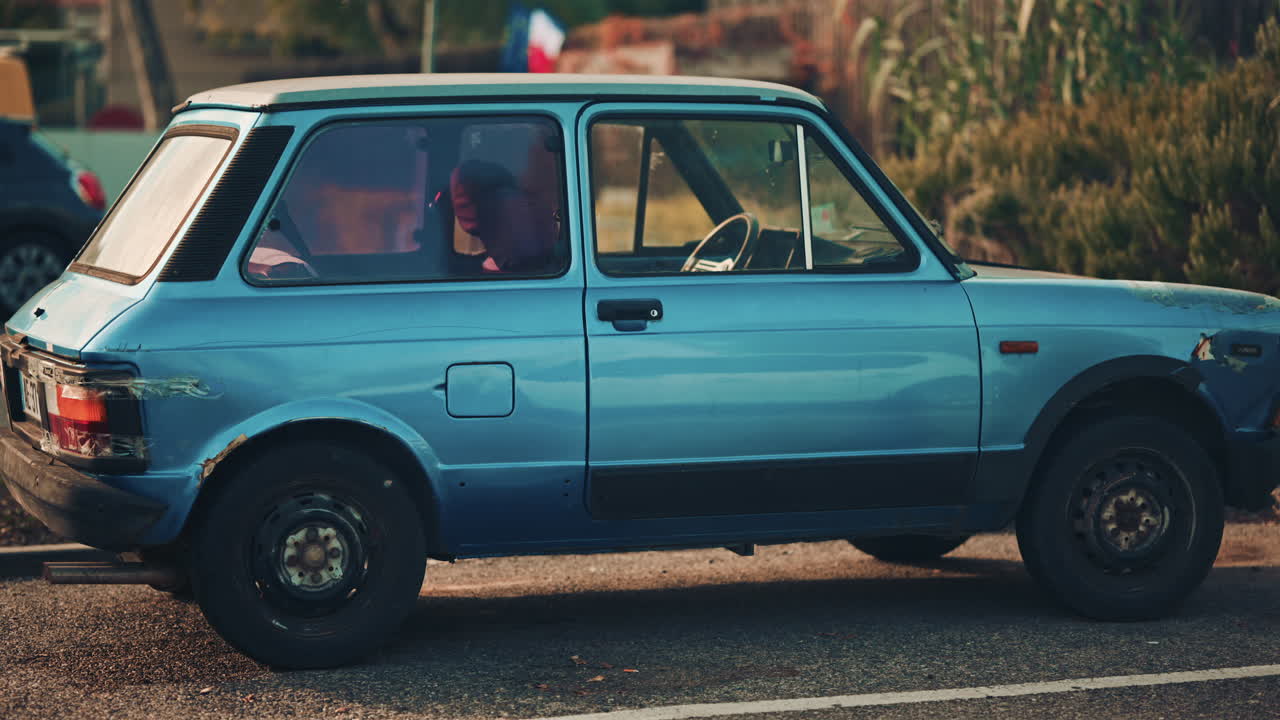 Side view of an old blue compact car with visible wear and rust parked