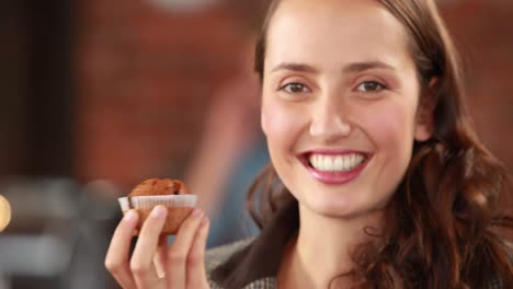 una chica hipster sonriente oliendo un cupcake