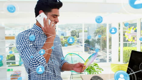 animación de iconos conectados sobre un hombre biracial hablando por teléfono celular sosteniendo la paleta de colores en la oficina.