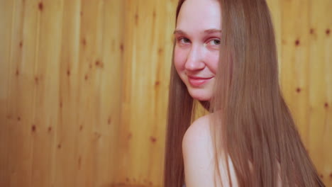 close up of young woman turning to camera and striking stylish pose while friend sits beside her on wooden sauna bench casting sideways glance gentle smile warm spa vibe and relaxed wellness mood