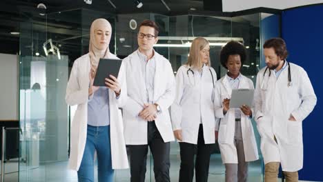 multiethnic doctors team walking and discussing coronavirus infection while typing on tablet in hospital