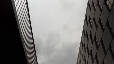 timelapse looking up between modern buildings as dark clouds race overhead