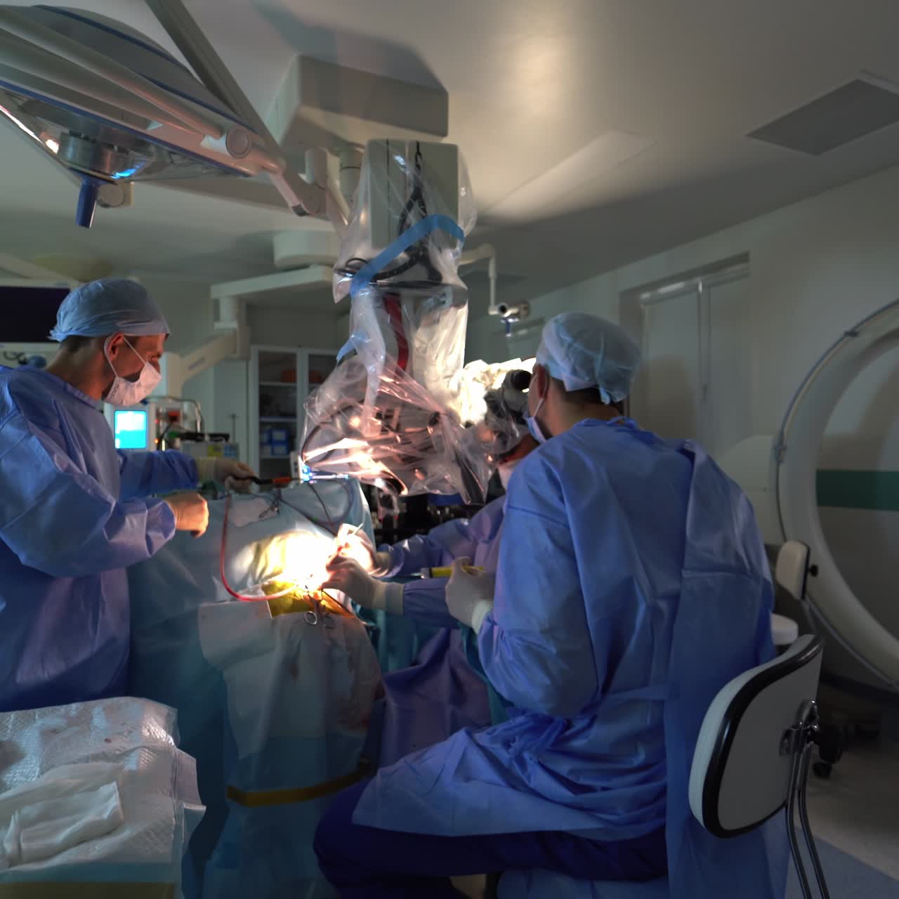 Spacious light surgical room with operation being held in it. Group of surgeons operating the patient. Monitors working at the backdrop