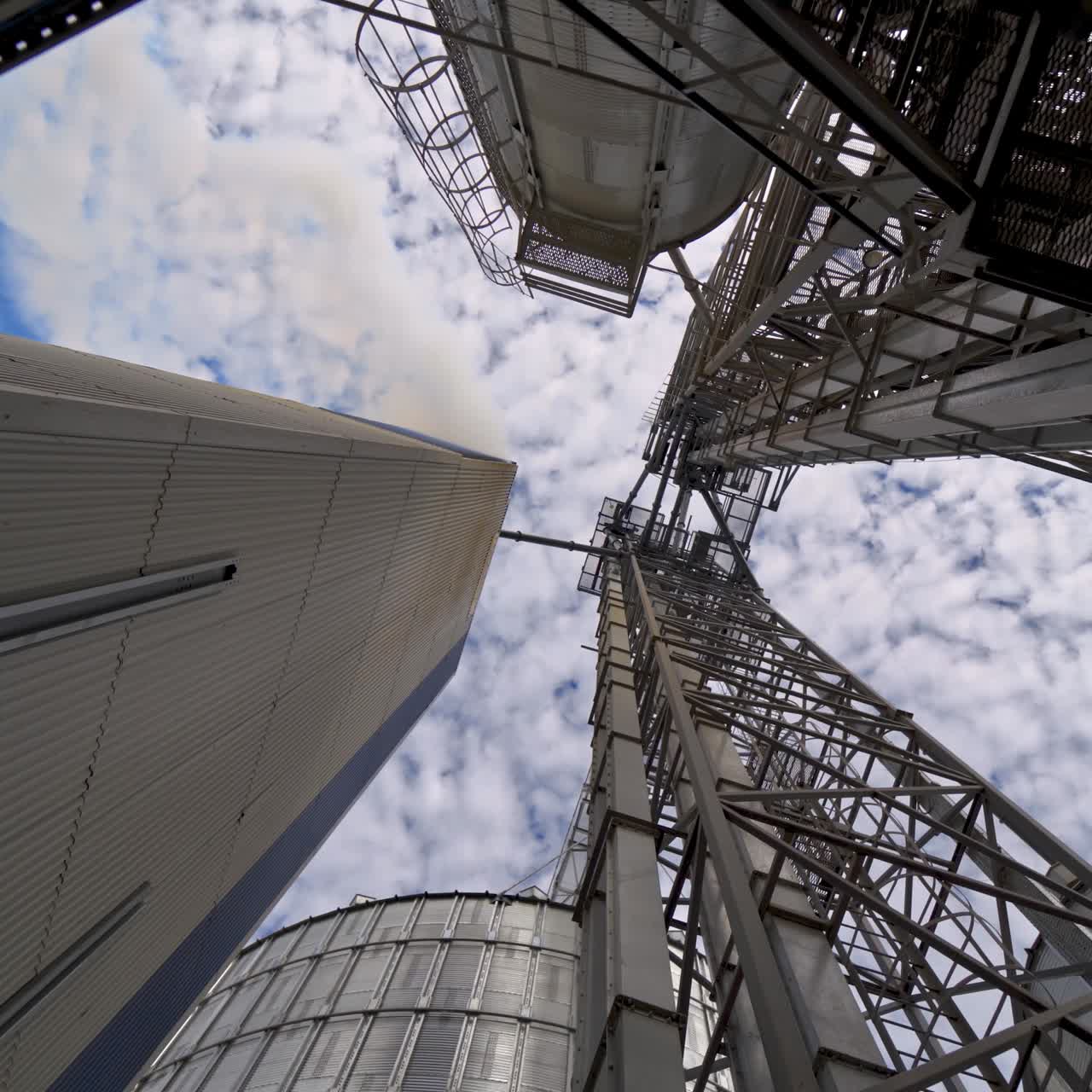 Industry. High metal stairs on the industrial plant. Modern territory for grain storage. Steel frame on warehouse outdoors. View from below.