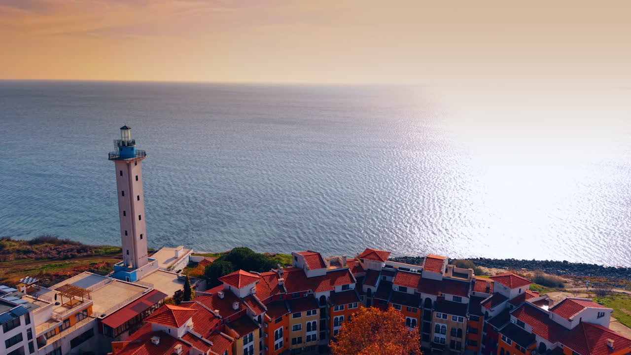 Filmato sopra i tetti rossi del complesso di Marina Cape e del faro adiacente. Avvicinamento all'infinito paesaggio marino del Mar Nero abbagliato dalla luce del sole al tramonto