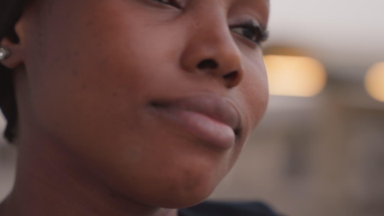 black woman closeup rooftop warm smile and engagement. soft golden light, visible dimples, steady eye contact, candid gestures, subtle laughter and speaking motion, urban evening scene of storyteller