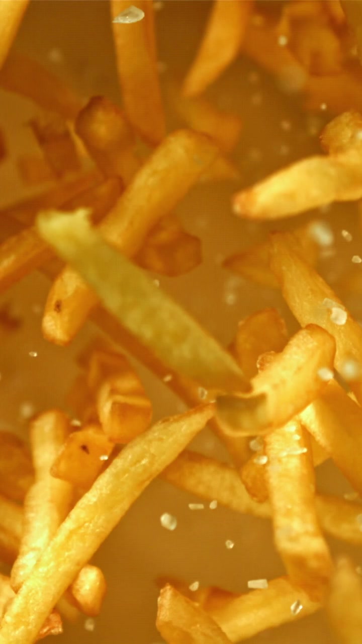 Primer plano a cámara lenta de sal cayendo sobre patatas fritas doradas