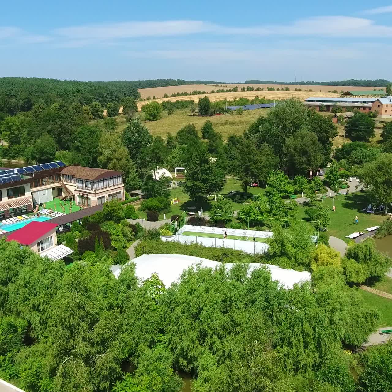 Sunlit green territory of beautiful spa resort in the countryside. Swimming-pool with people resting around it. Aerial perspective