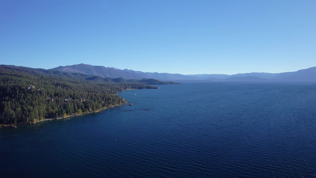 Ampla imagem de drone mostrando um ambiente de lago tranquilo com floresta natural e montanhas ao fundo. Lago Tahoe.