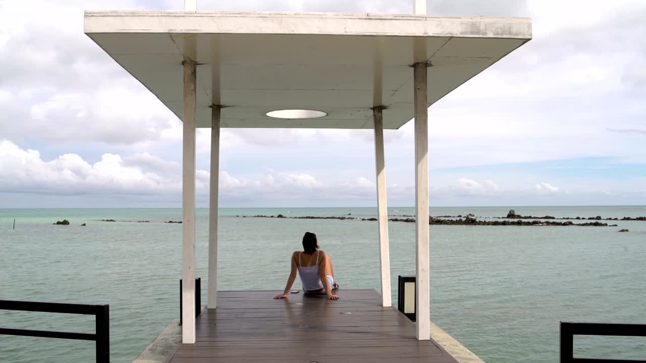 A woman looks at the sea sitting on the pier