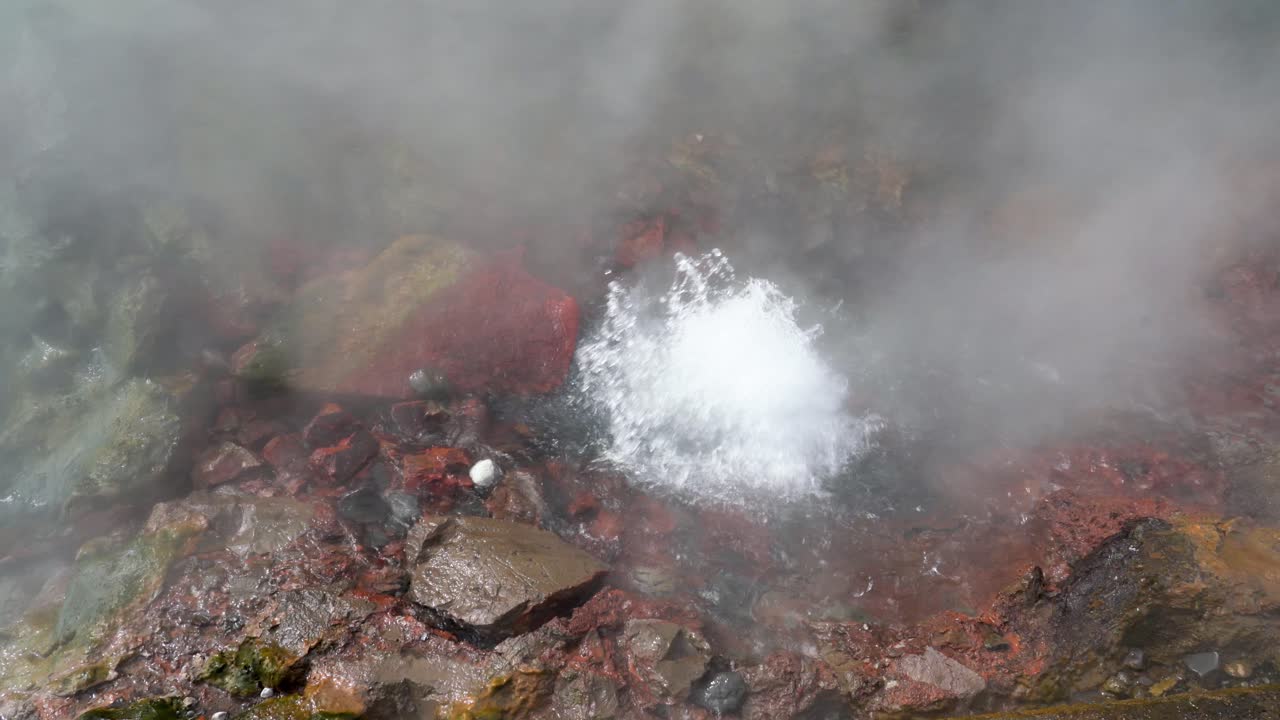 Splashing geothermal hot spring in Iceland, close up shot. Hot steam rising up.