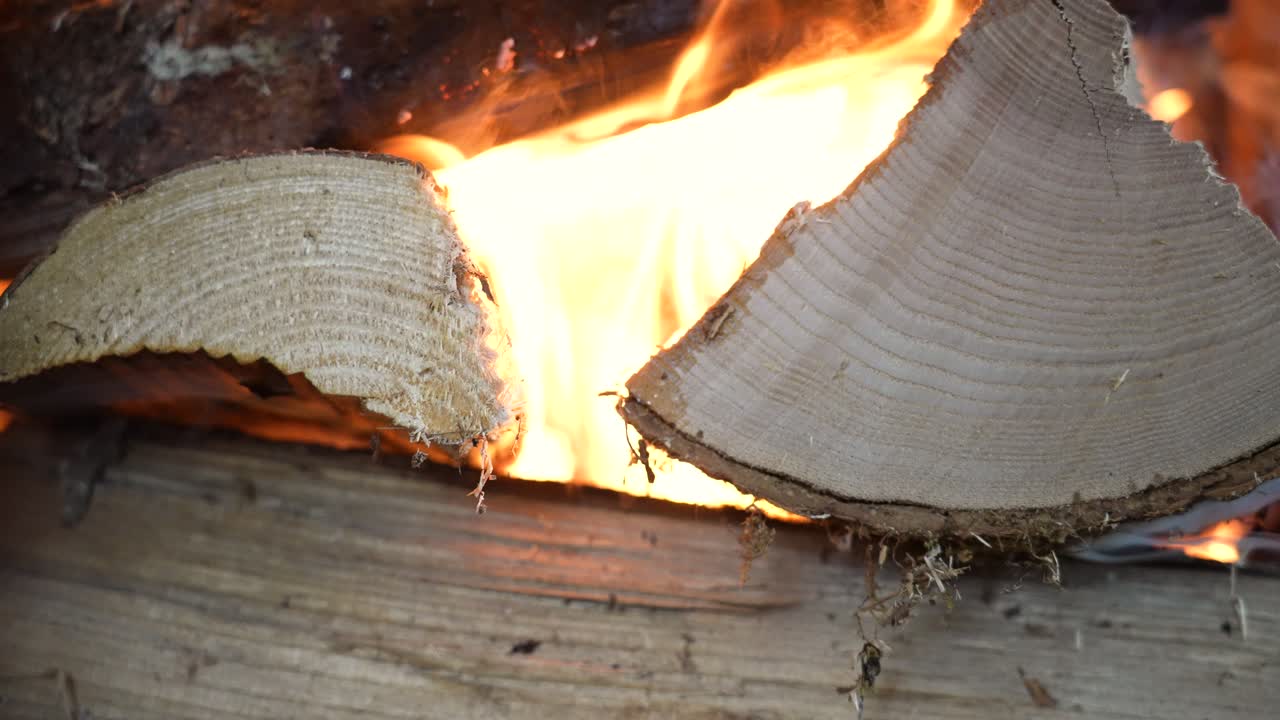 Rekaman gerak lambat gaya makro api melahap tumpukan kayu bakar di dalam perapian. Kamera menangkap garis-garis halus tekstur kayu saat nyala api bergulir perlahan di atas permukaan