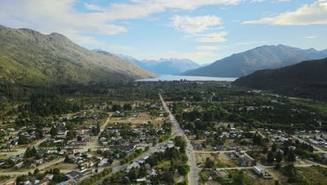 dolly out flying over lago puelo village surrounded by pine tree woods with lake and andean mountains in background at sunset, chubut, patagonia argentina