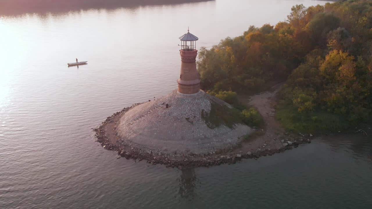 Orbiting footage around the old stone lighthouse on the Danube river with sunset in the background and amazing autumn colors on the forest