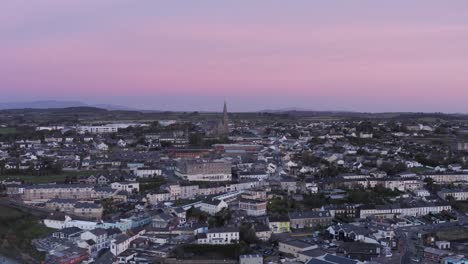 Cielo-Rosa-Amanecer-Aéreo-Se-Eleva-Sobre-La-Ciudad-Costera-De-Tramore,-Irlanda