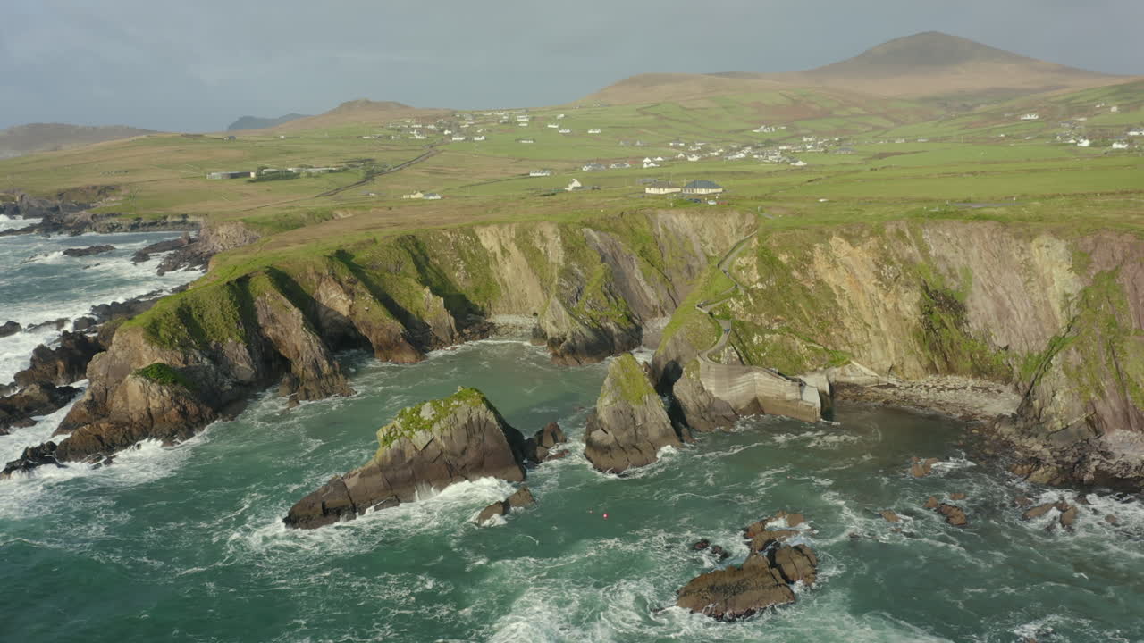 Vista aérea, el Muelle de Dunquin se encuentra en una pequeña bahía aislada rodeada de acantilados rocosos, famosa imagen de postal de Irlanda, el paisaje circundante es una atractiva mezcla de montañas y cimas de acantilados.