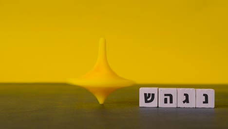 a plastic top spins and wobbles to a stop beside the four hebrew letters nun, gimel, heh and shin shown against a two-tone background