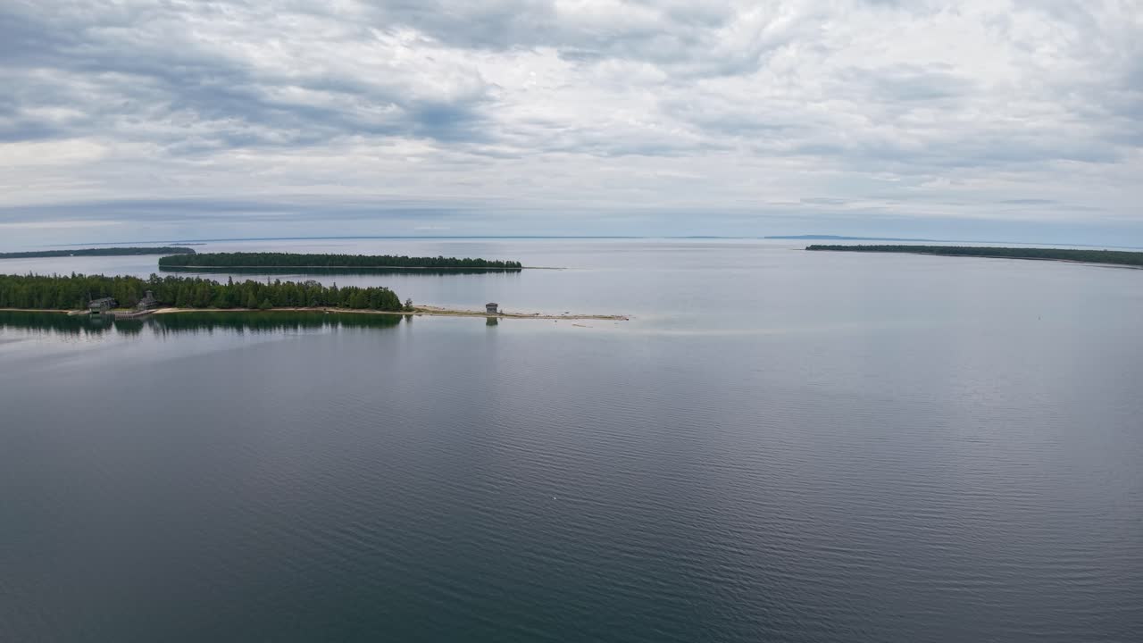 Drone footage of calm water with cloudy skies reflecting over Michigan’s Les Cheneaux Islands shoreline