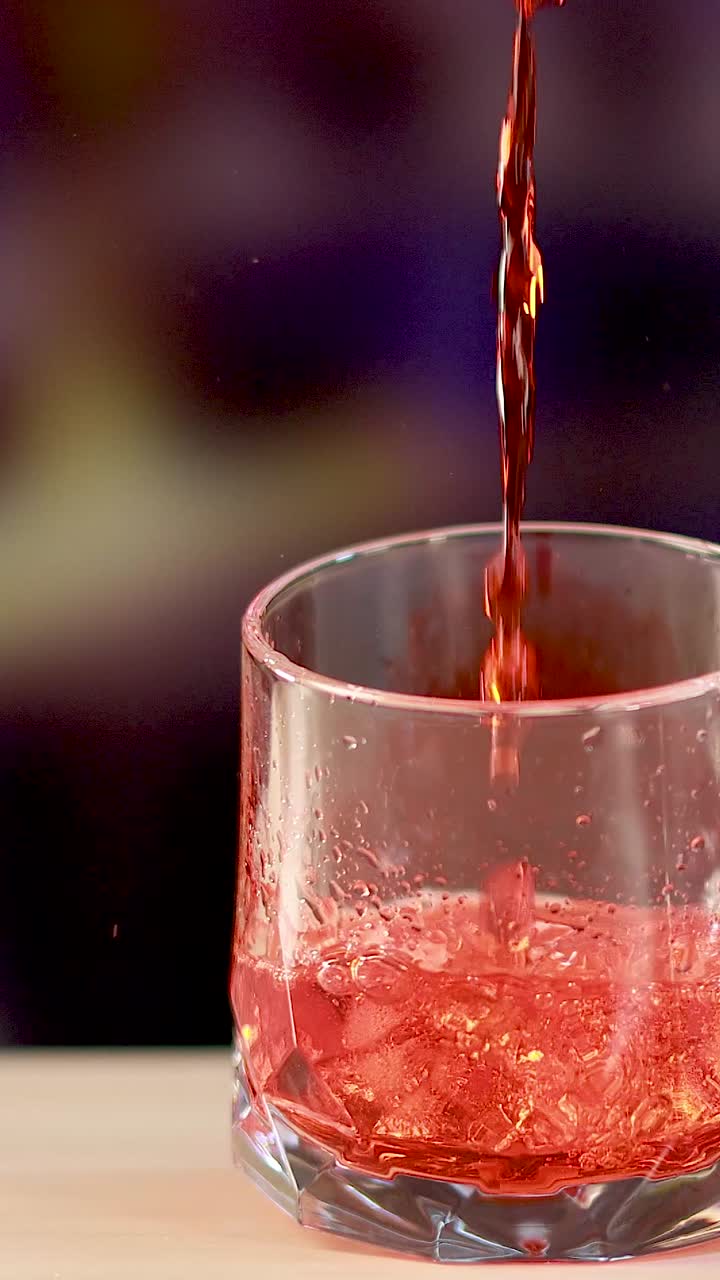 A Negroni cocktail is prepared by pouring red liquid over ice in a glass, set against a colorful background