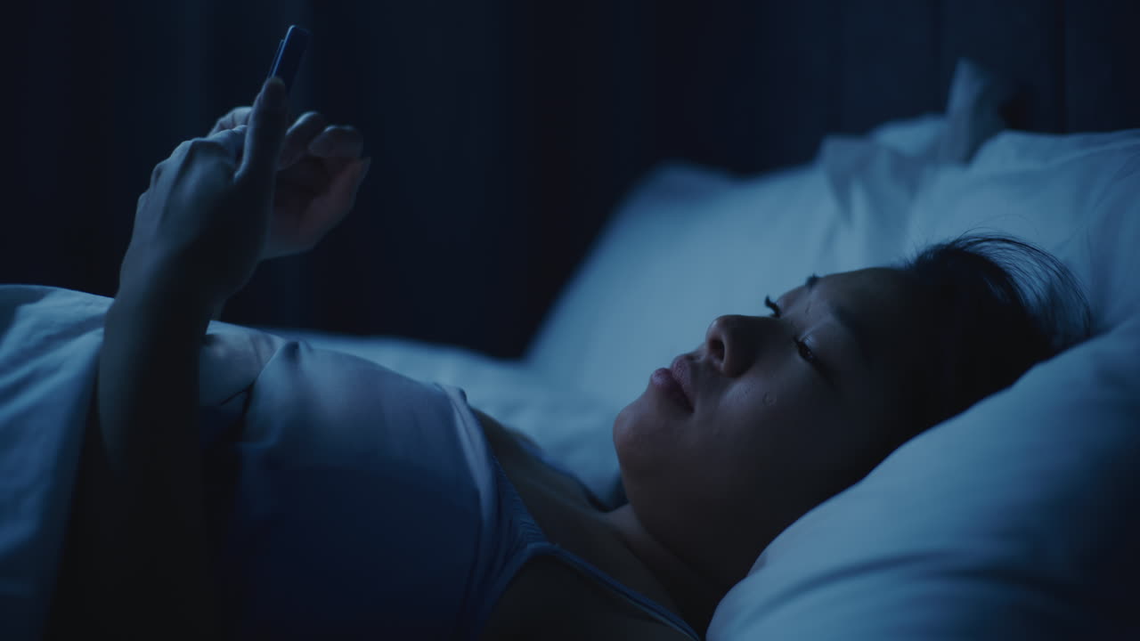 밤에 침대에서 스마트폰을 사용하는 여성