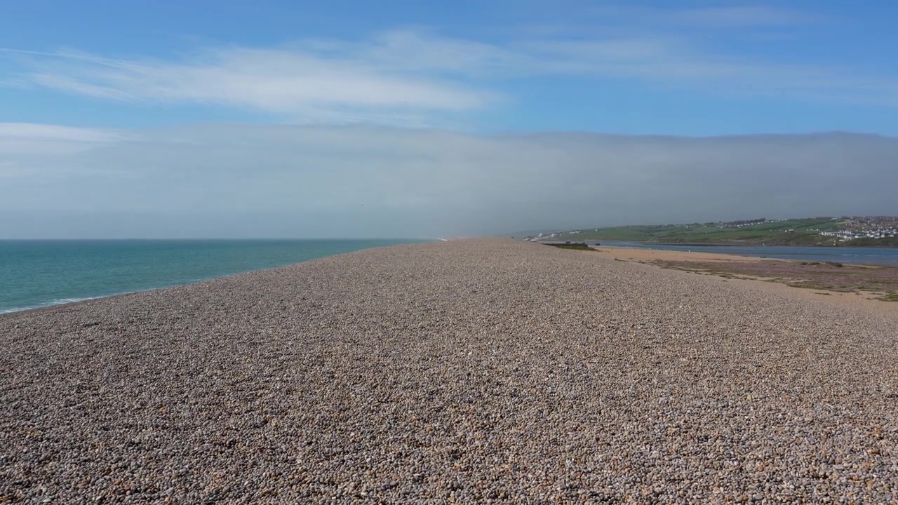 Ein weitläufiger, kinoreifer Blick auf die ikonische Kiesbank Chesil Beach in Dorset, die den riesigen Kiesrücken zwischen dem Meer und der Fleet-Lagune zeigt.