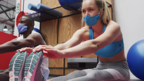 personas en forma con máscaras faciales realizando ejercicios de estiramiento en el gimnasio