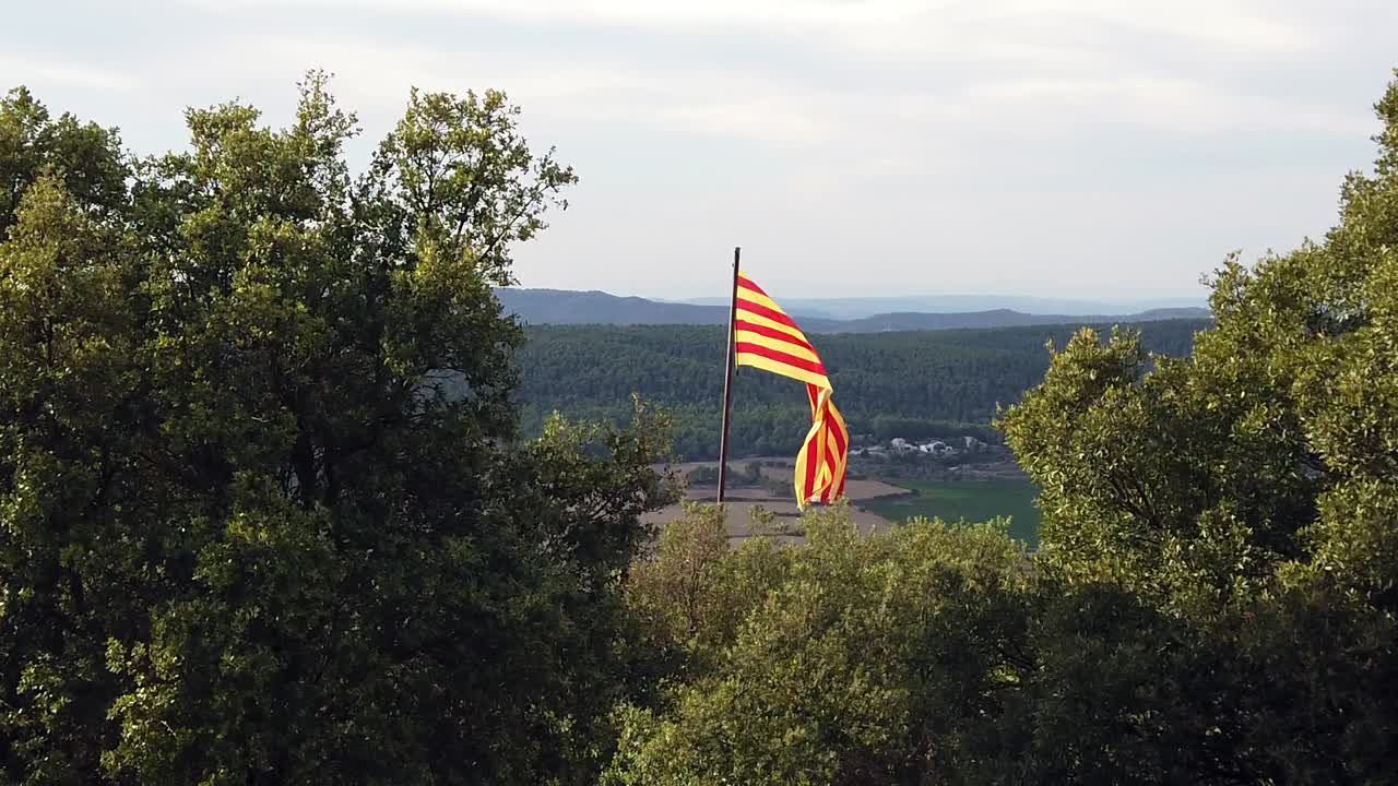 cámara lenta de la bandera catalana en la cima de una colina, con vistas a las colinas con un cielo nublado