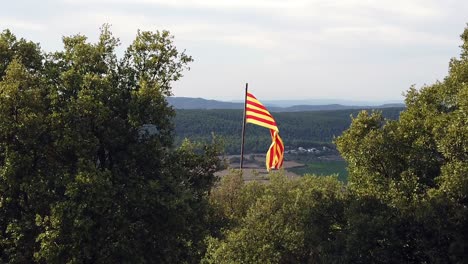 Cámara-Lenta-De-La-Bandera-Catalana-En-La-Cima-De-Una-Colina,-Con-Vistas-A-Las-Colinas-Con-Un-Cielo-Nublado