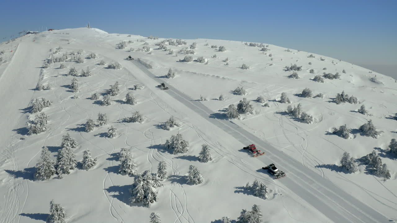Snow groomers preparing a pristine ski slope on a snowy mountain