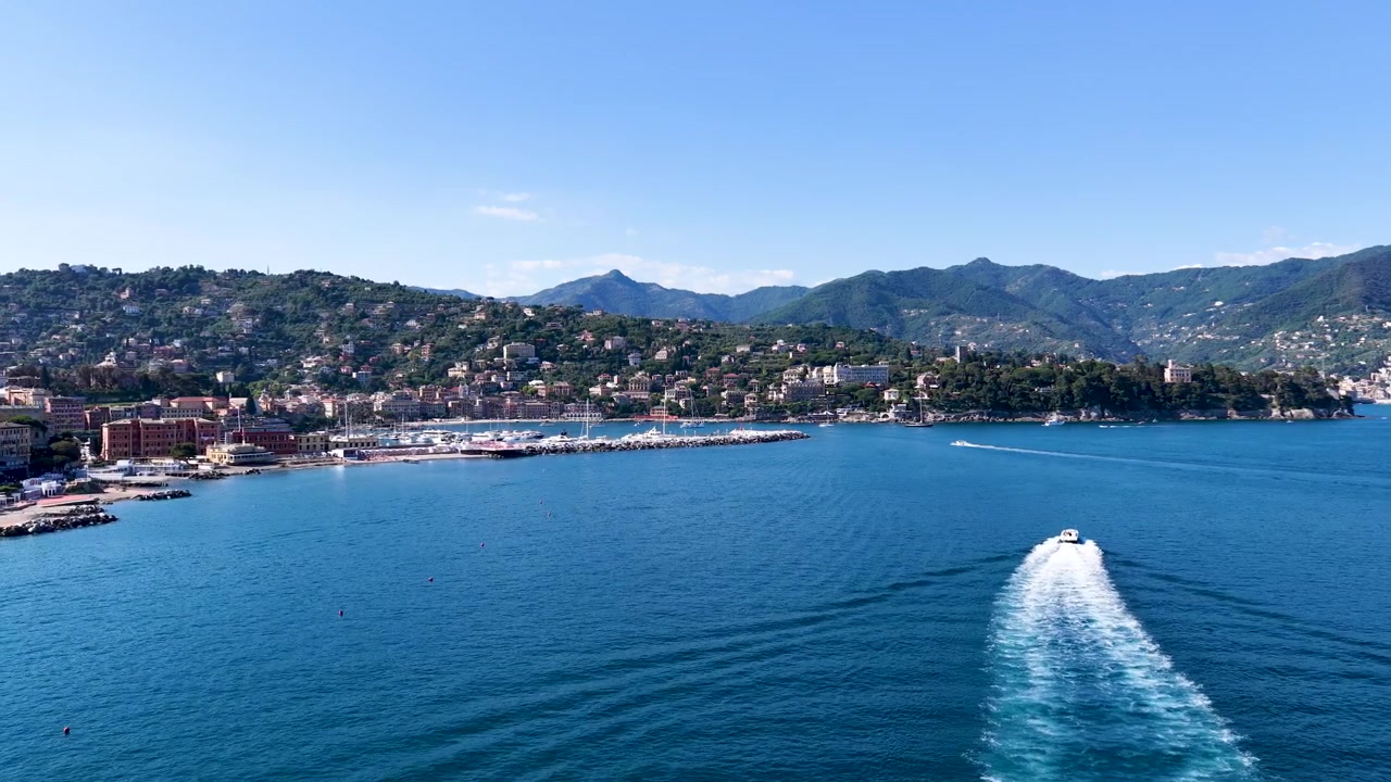 Ripresa aerea con drone dall'alto segue un motoscafo bianco che lascia una scia sulle acque blu del Mediterraneo.