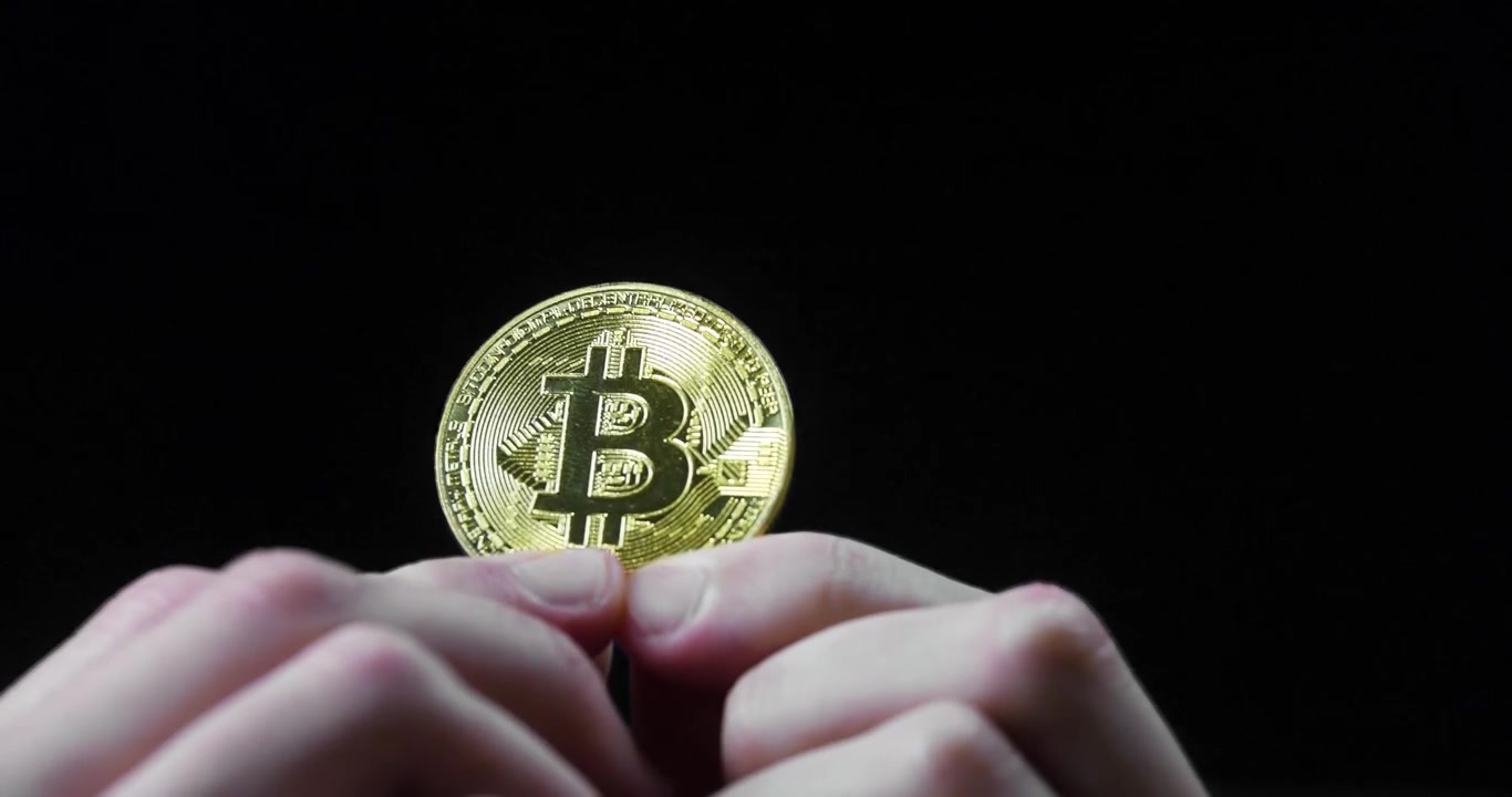 Duas mãos segurando uma criptomoeda Bitcoin em fundo preto, simbolizando tecnologia financeira.