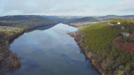 Flug-In-Geringer-Höhe-Einen-Fluss-Hinauf-Mit-Häusern-Auf-Der-Klippe