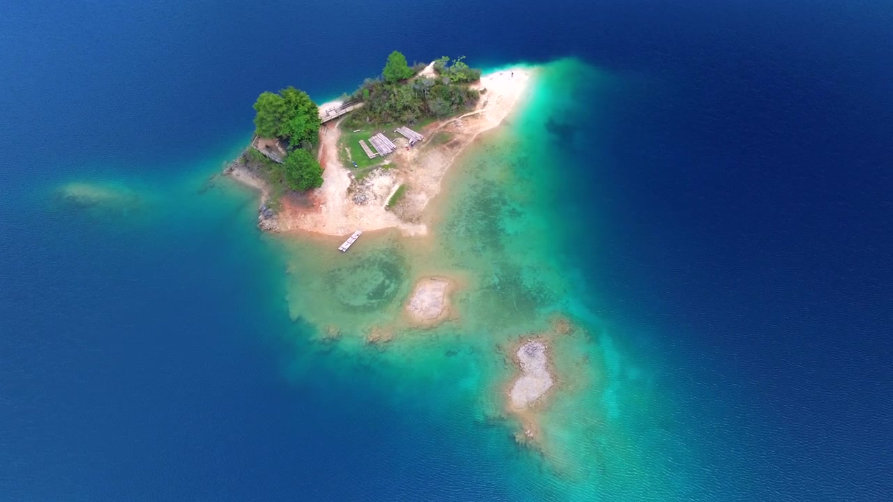 Ripresa aerea statica dall'alto con drone di una piccola isola con sabbia bianca e acque basse turchesi, circondata da un lago blu profondo in Chiapas, Messico