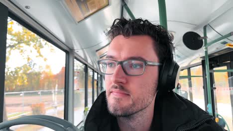 Un-Encantador-Hombre-Europeo-Con-Barba-Y-Gafas-Disfruta-De-Su-Viaje-Como-Pasajero-De-Autobús-En-Alemania,-Capturando-Su-Vibrante-Experiencia-Con-Un-Selfie-Espontáneo-Hacia-La-Cámara.