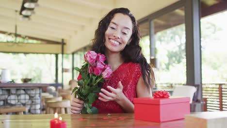 Happy-biracial-woman-with-roses-making-valentine's-day-video-call,-sending-kisses