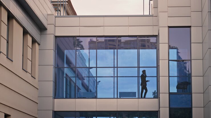 Silhouette di un uomo che cammina davanti alla finestra di un edificio per uffici moderno. Uomo d'affari sconosciuto