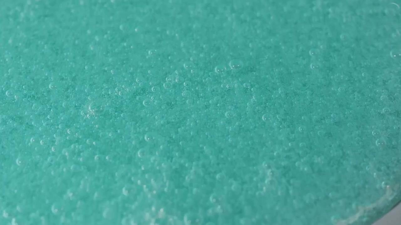Primo piano di gel turchese che si espande con bolle su superficie grigia