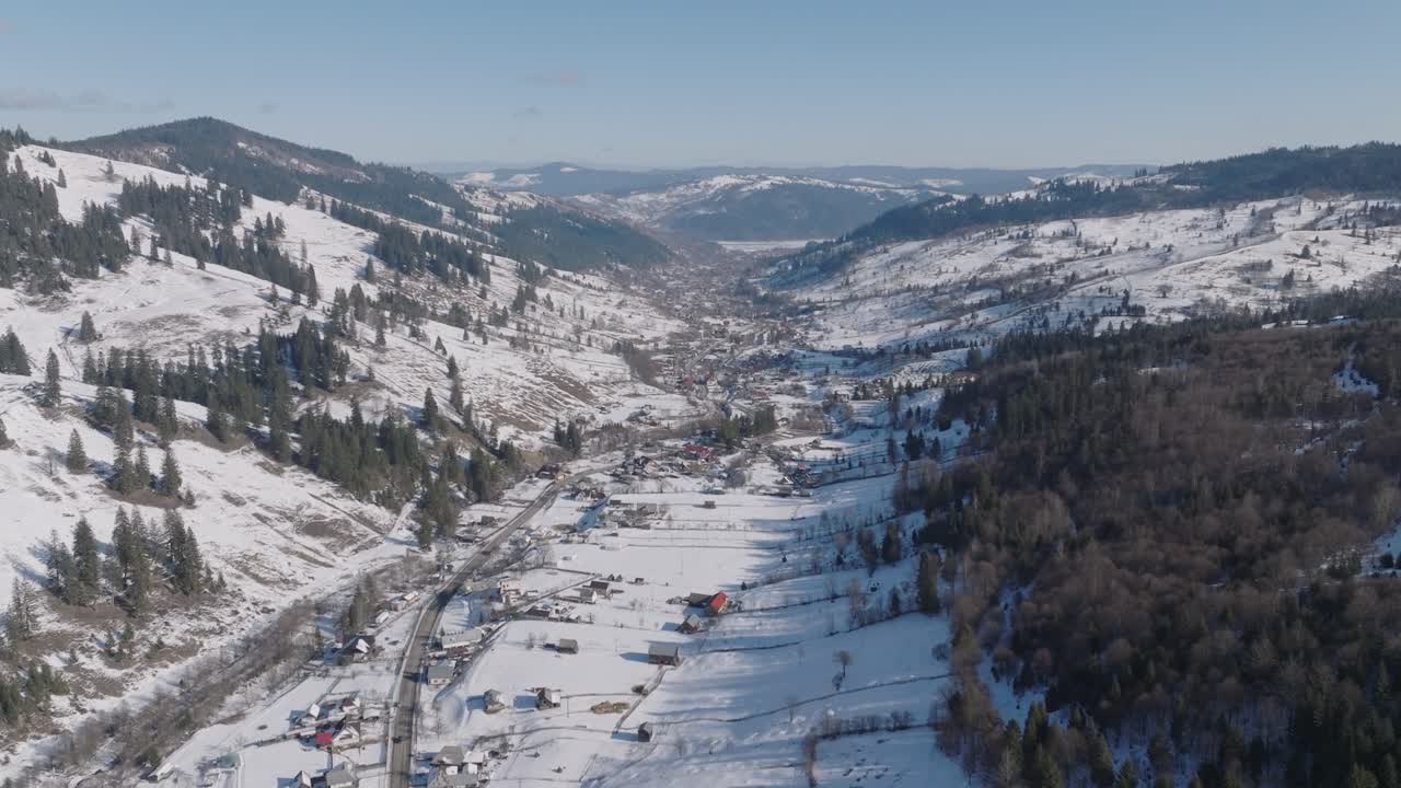 un pueblo de valle nevado rodeado de montañas boscosas en un claro día de invierno, vista aérea