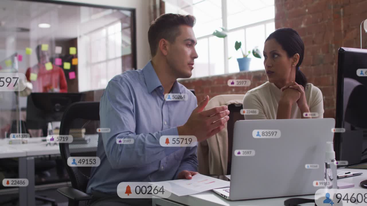 Man leaning and speaking while woman reading report, alerts appearing over laptop for business
