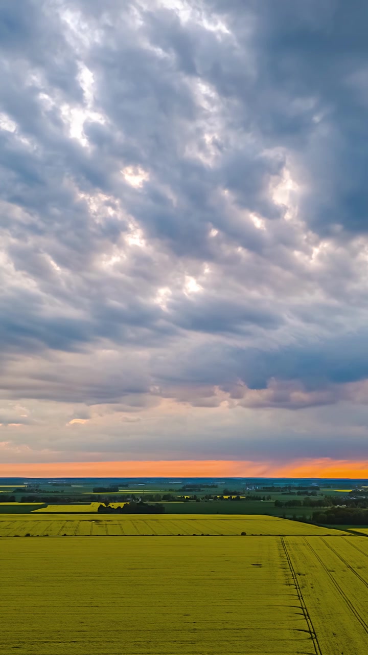 Expansive farmland beneath dramatic layered clouds at sunset, aerial vertical timelapse with glowing soft light