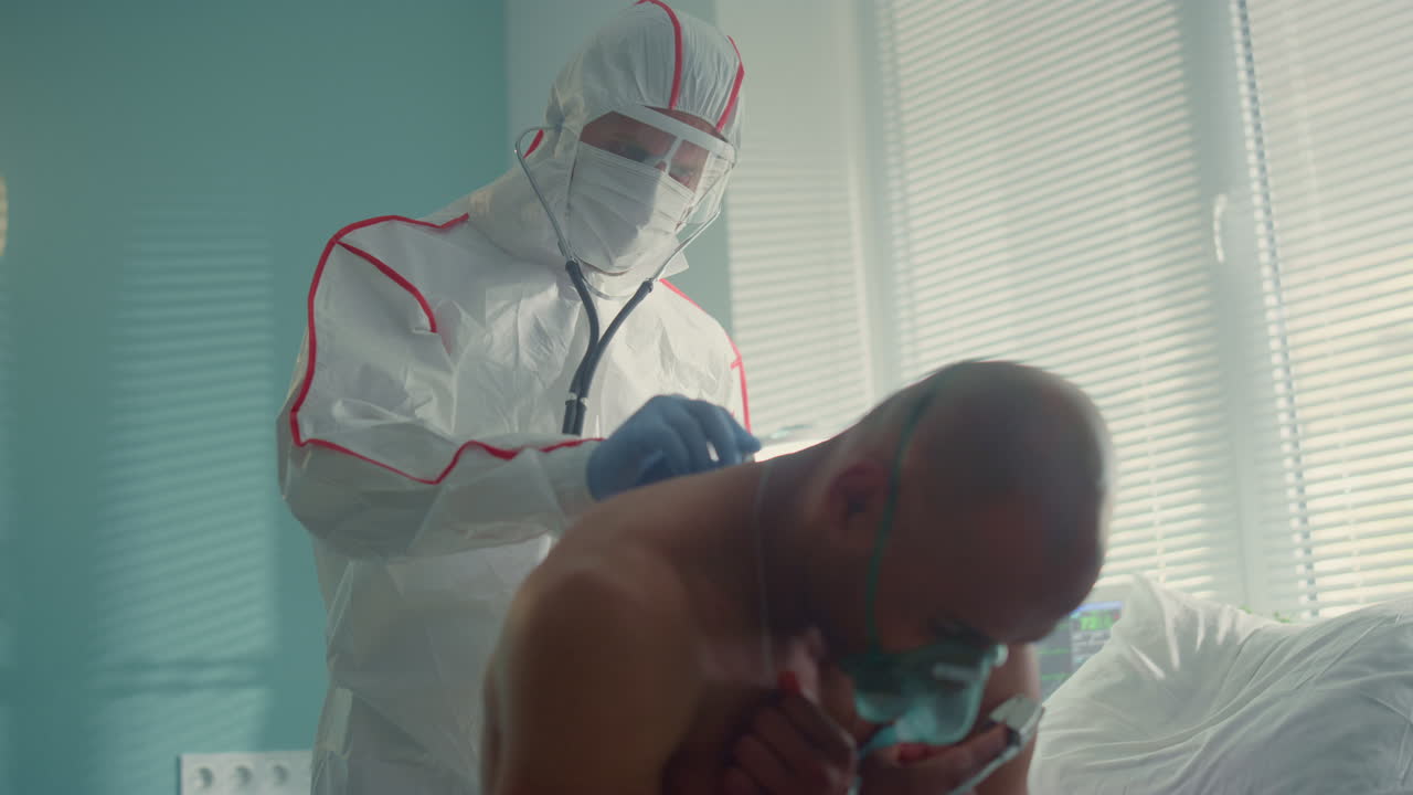 el médico examina la espalda del paciente de covid-19 con un estetoscopio en una máscara de traje protector.