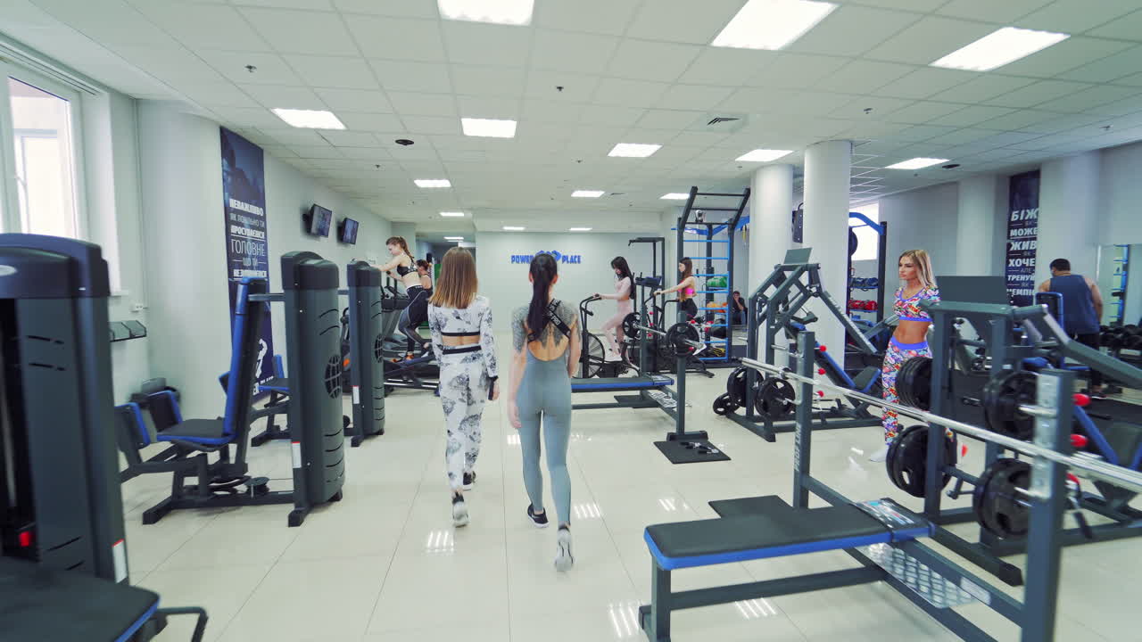 Group of young sporty women at the end of workout in a sports club. Beautiful females in sport clothes going out of a fitness center after hard training on the modern simulators.