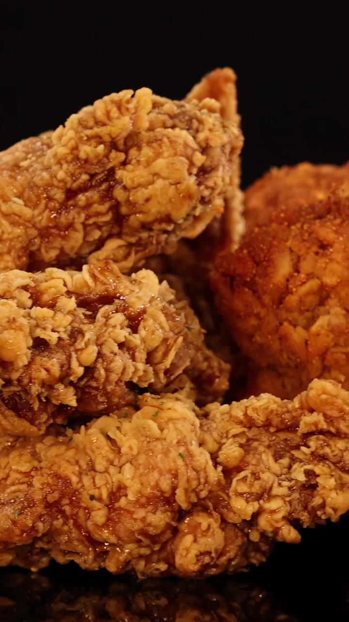 Golden fried chicken wings, drumsticks, and nuggets rotate on a reflective surface under warm studio lighting, highlighting crunchy textures and appetizing details